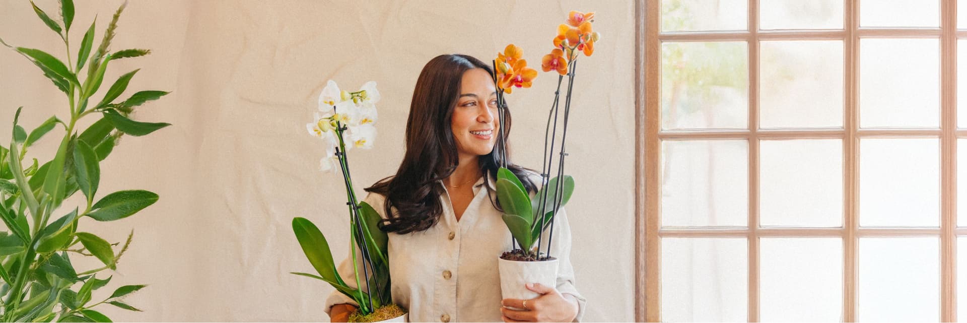 A woman smiles while holding two beautiful orchid plants in stylish pots.