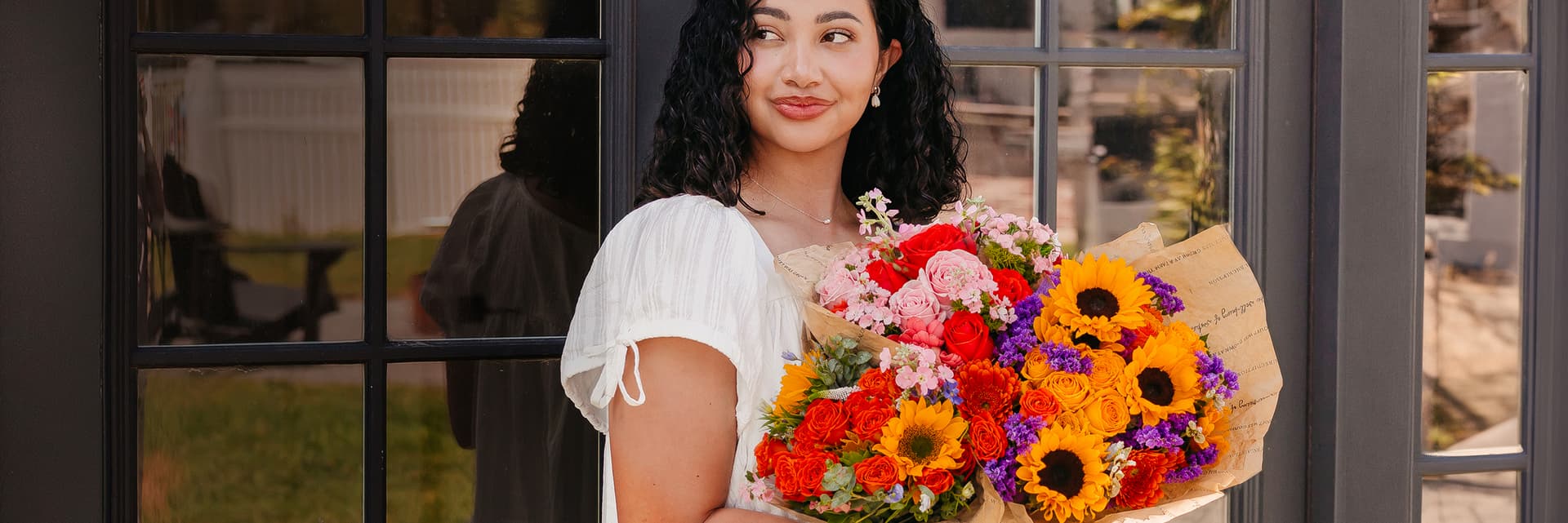 A smiling woman holds a vibrant bouquet of sunflowers and mixed flowers, perfect for any occasion.